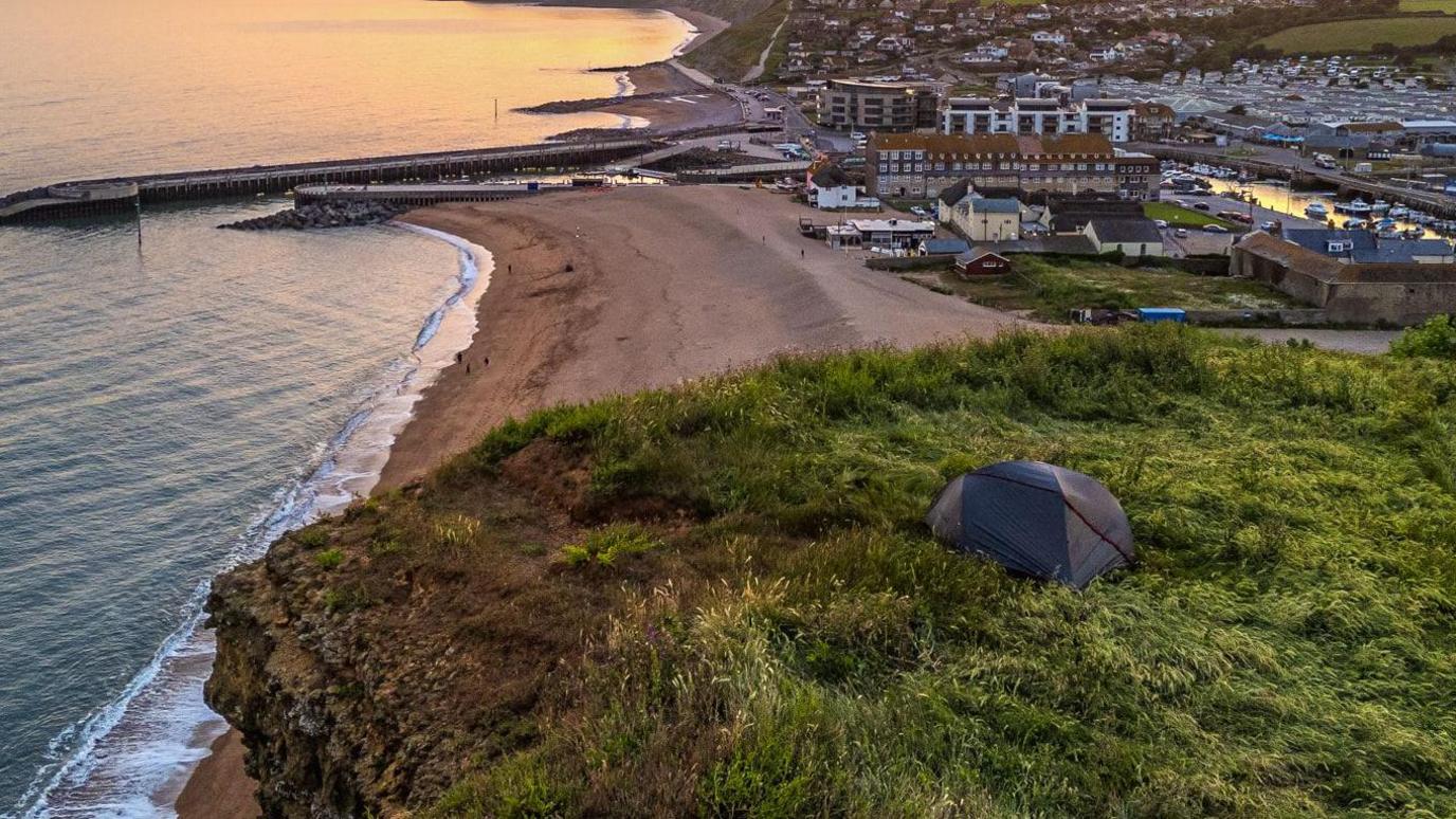 Tent on cliff, with town in background