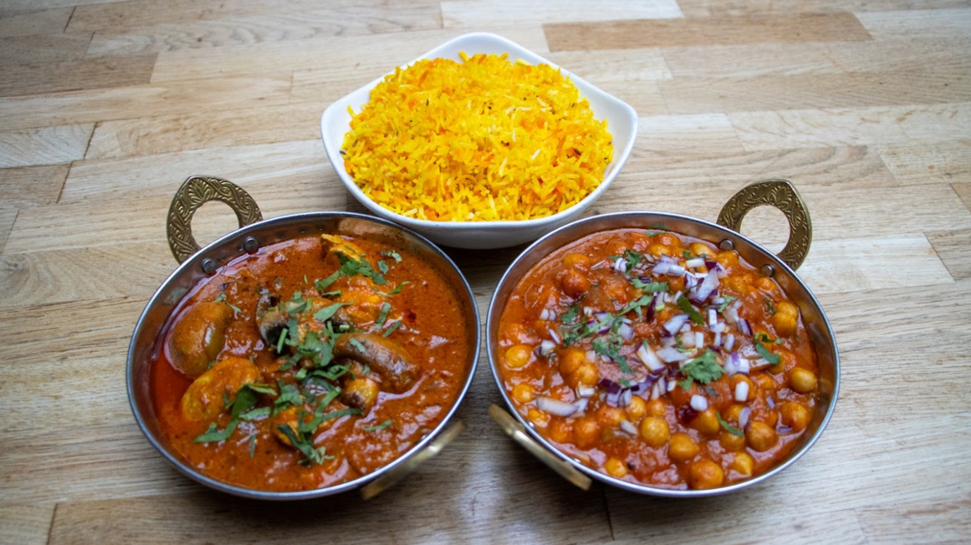 Three bowls of food are sat on a table. One is yellow rice, two are curry dishes