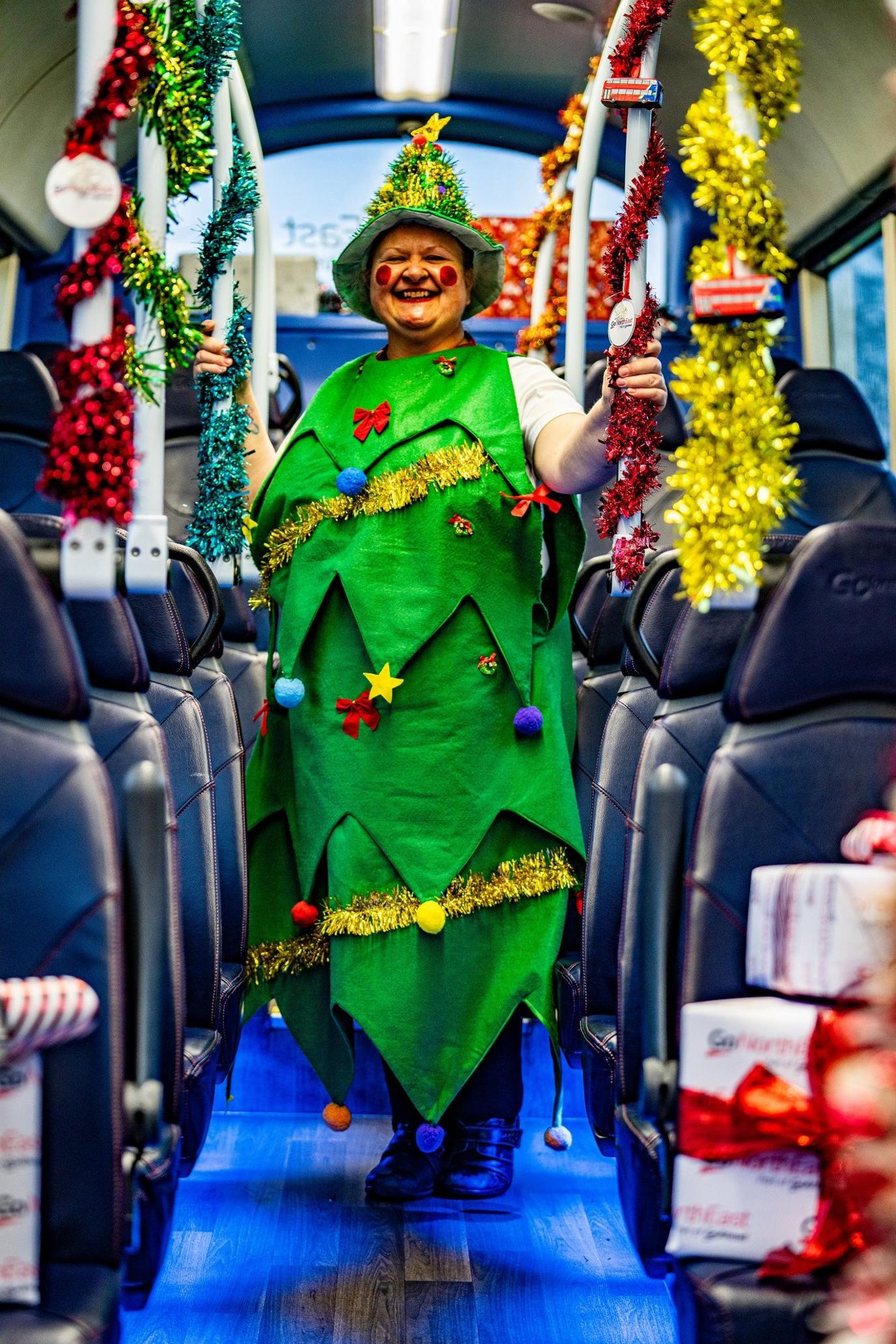 Julie Richardson standing on a bus dressed as a Christmas tree. She has rosy red cheeks.