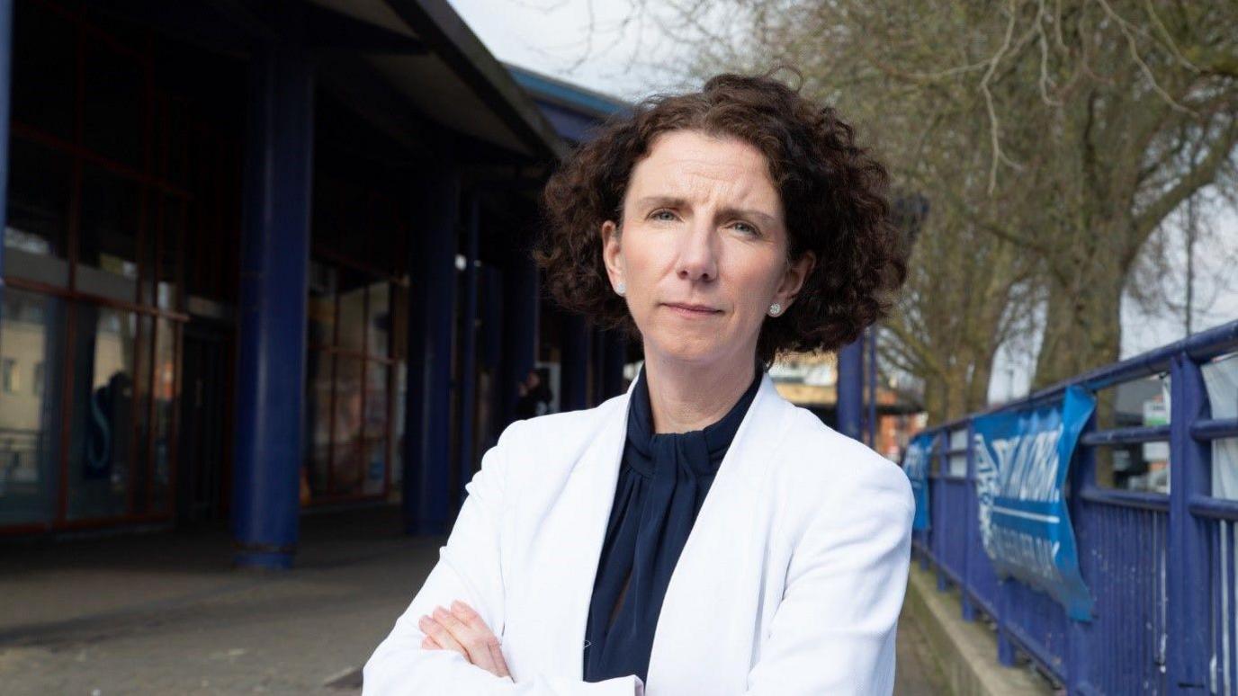 Anneliese Dodds MP outside Oxford railway station. She has her arms crossed in front of her chest.