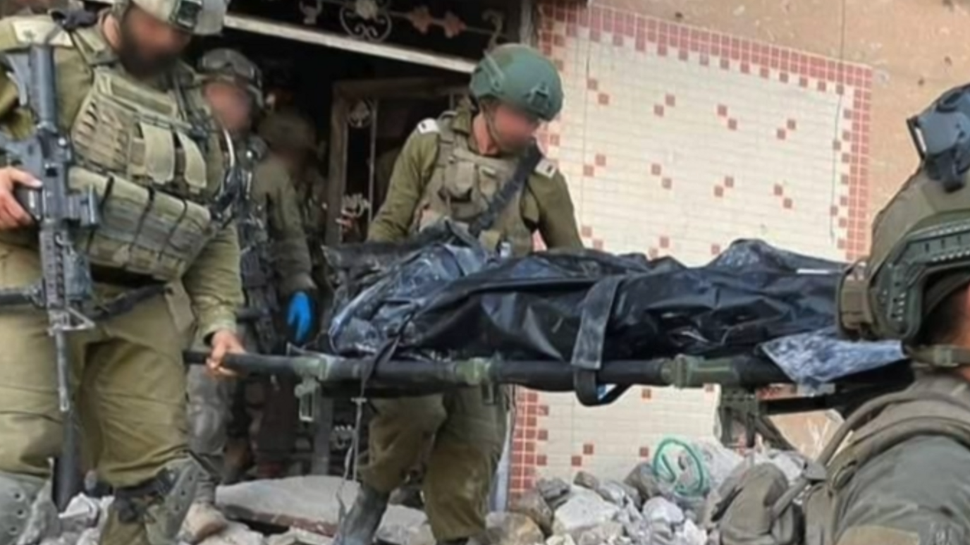 Israeli soldiers with their faced blurred carry a corpse in a black body bag, purportedly of Yahya Sinwar, out of a destroyed house which has distinctive tilework on the front. 