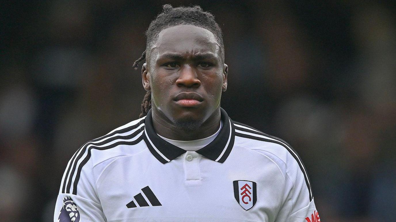 Calvin Bassey wears a white Fulham shirt with a stern expression on his face