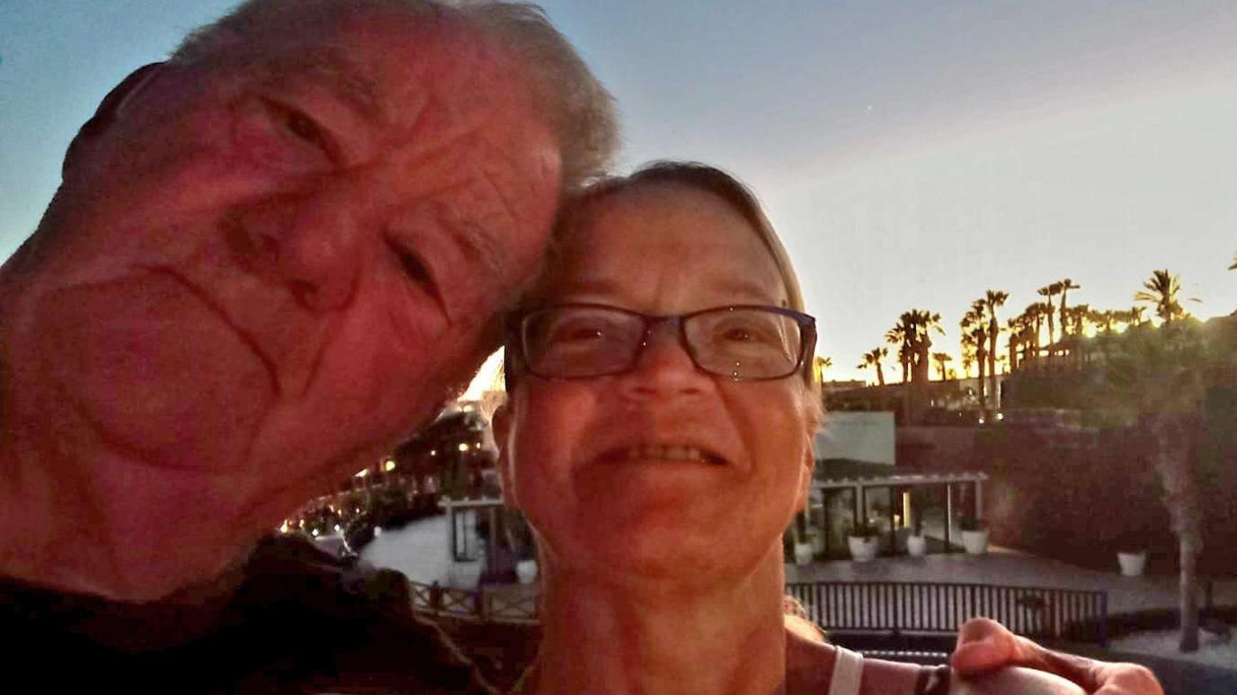 A selfie picture of Julie Green, 60, who has brown hair tied back and is wearing purple rimmed glasses, with Leslie Green, with a grey hair and a dark t-shirt.