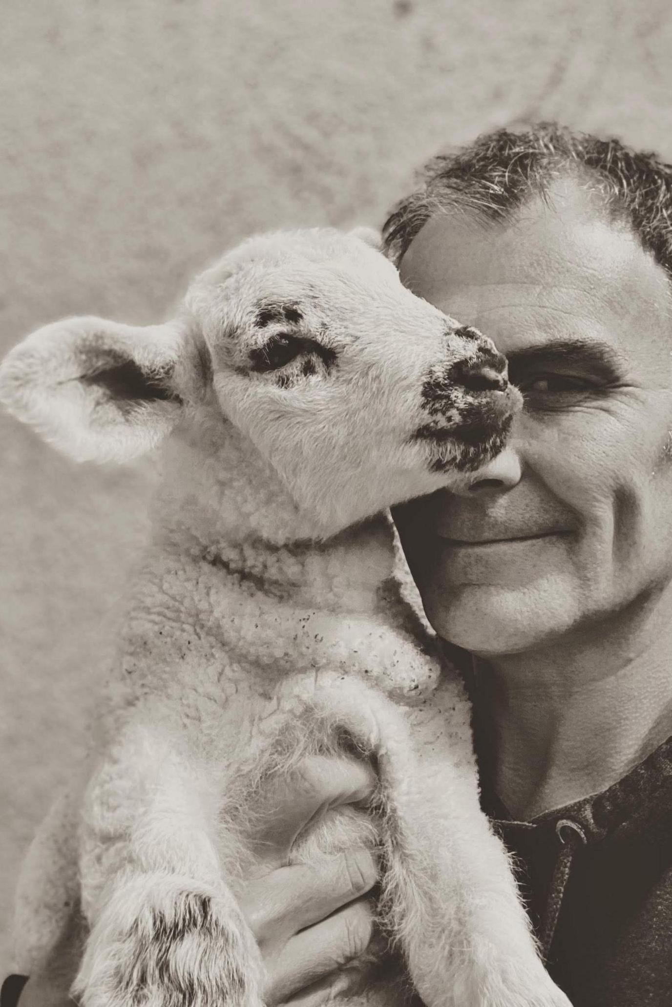 A black and white photo of Stephen giving Benny the lamb a cuddle