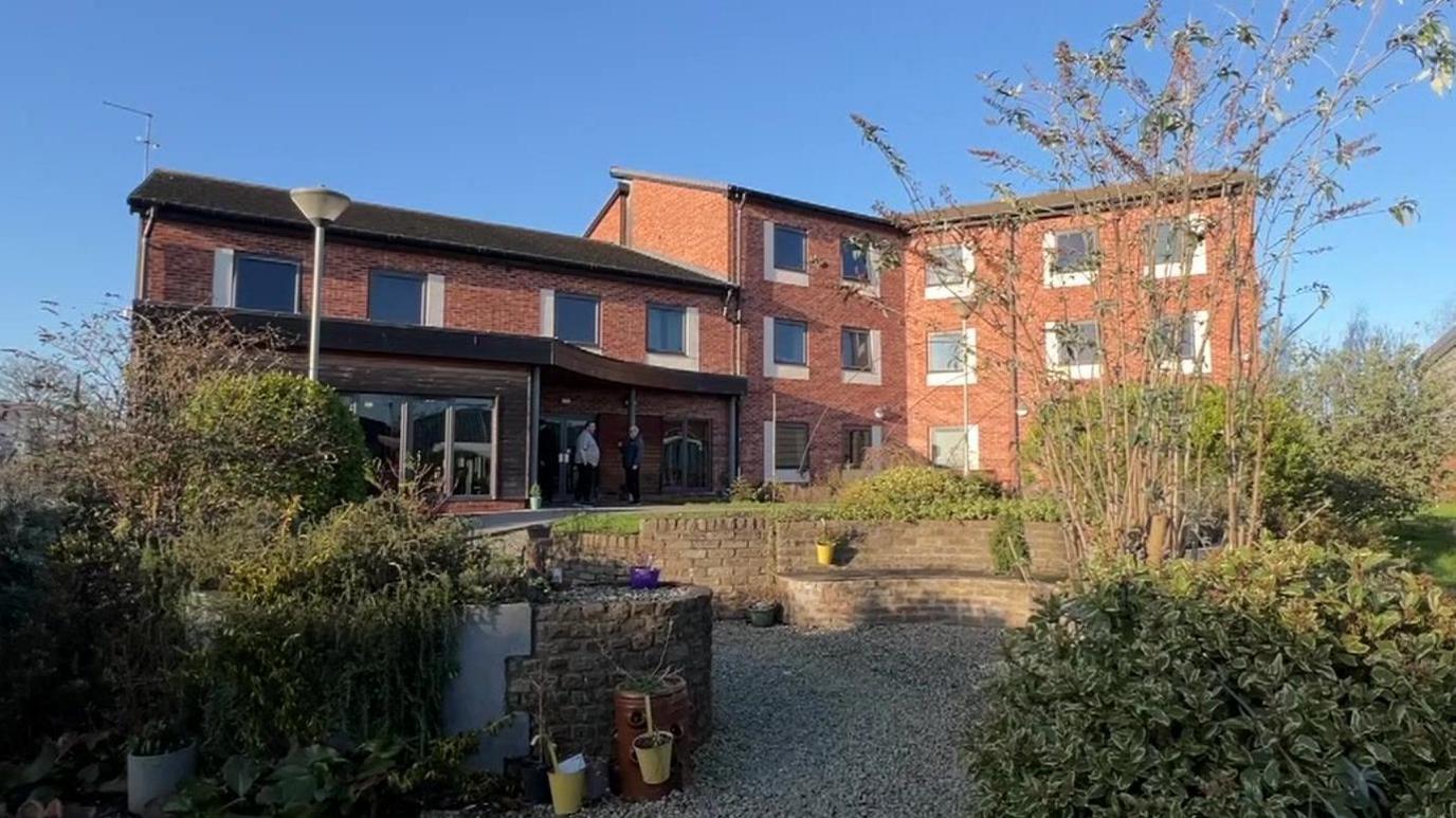 A brick-built accommodation block with a gravel garden at the front and small bushes