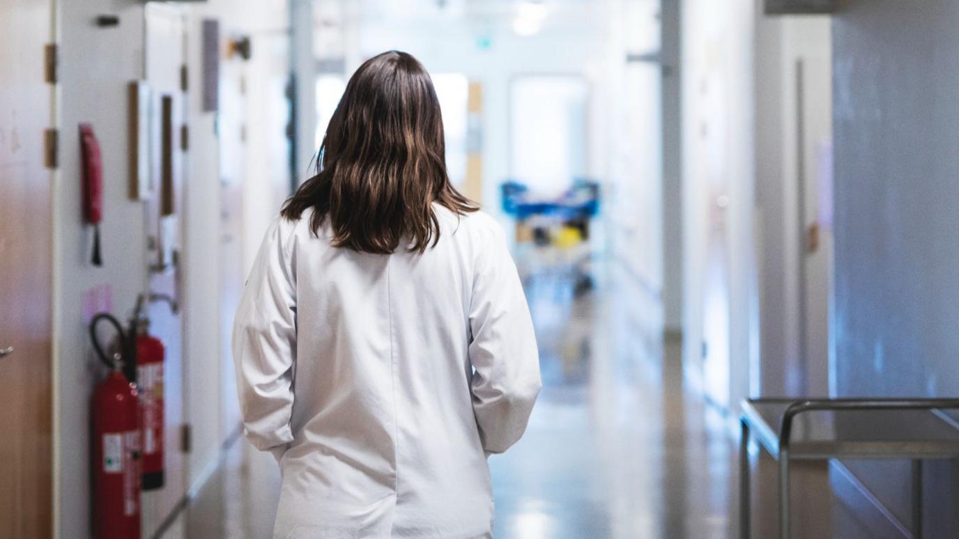 A doctor is seen walking away down a hospital corridor