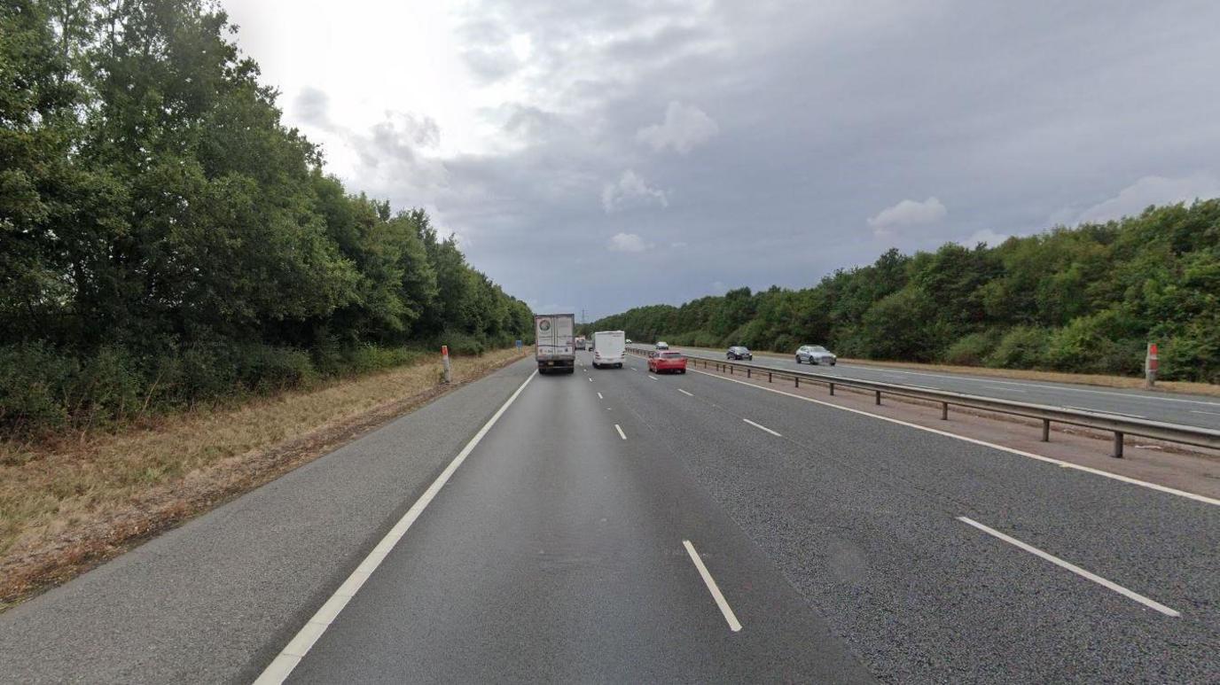 A road on an overcast day, vehicles are driving away from the camera in the left lanes. Some are driving in the opposite direction in the right lanes.