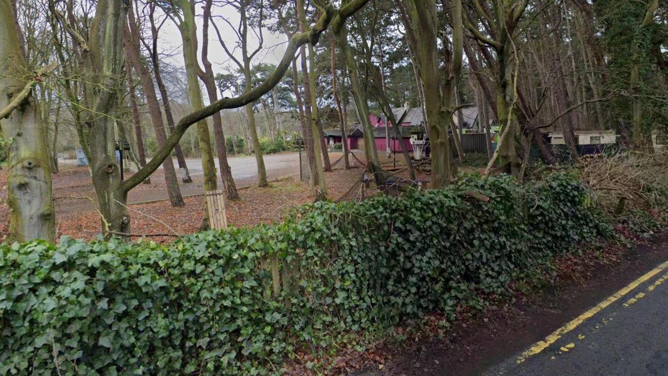The former nightclub building can be seen behind a hedge and a large number of trees.
