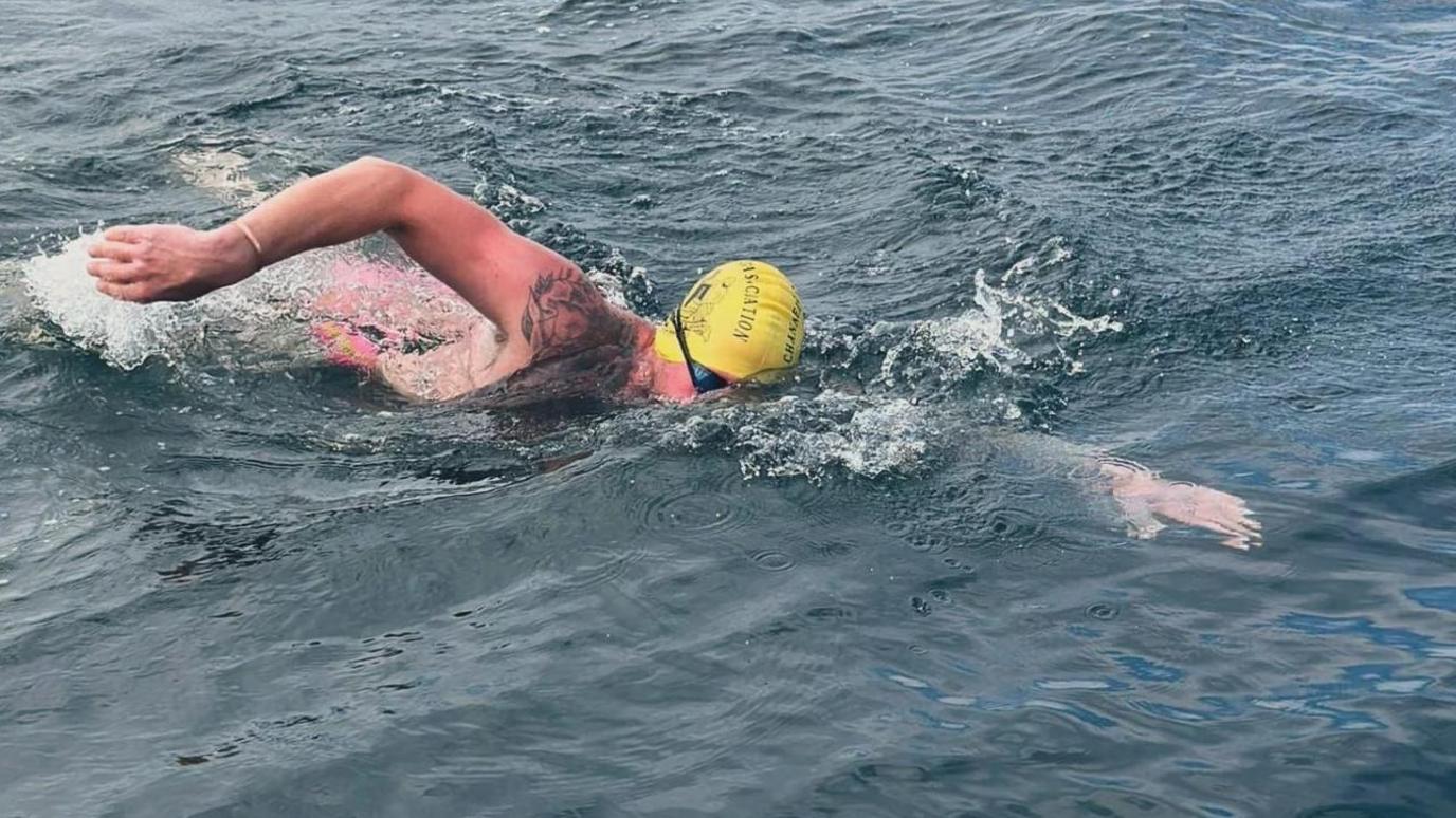 A man wearing a yellow swim cap and googles swimming in a rough sea