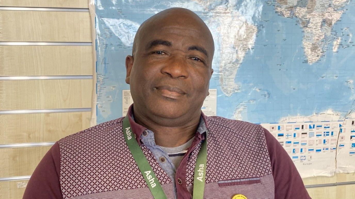 A man with a maroon T-shirt and a green lanyard reading 'Asha'