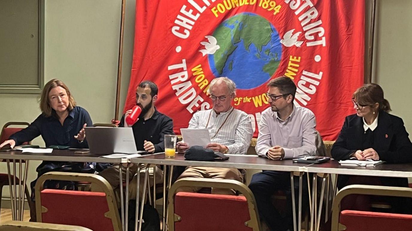 Image of councillors sitting at a table on one side, speaking to the room.