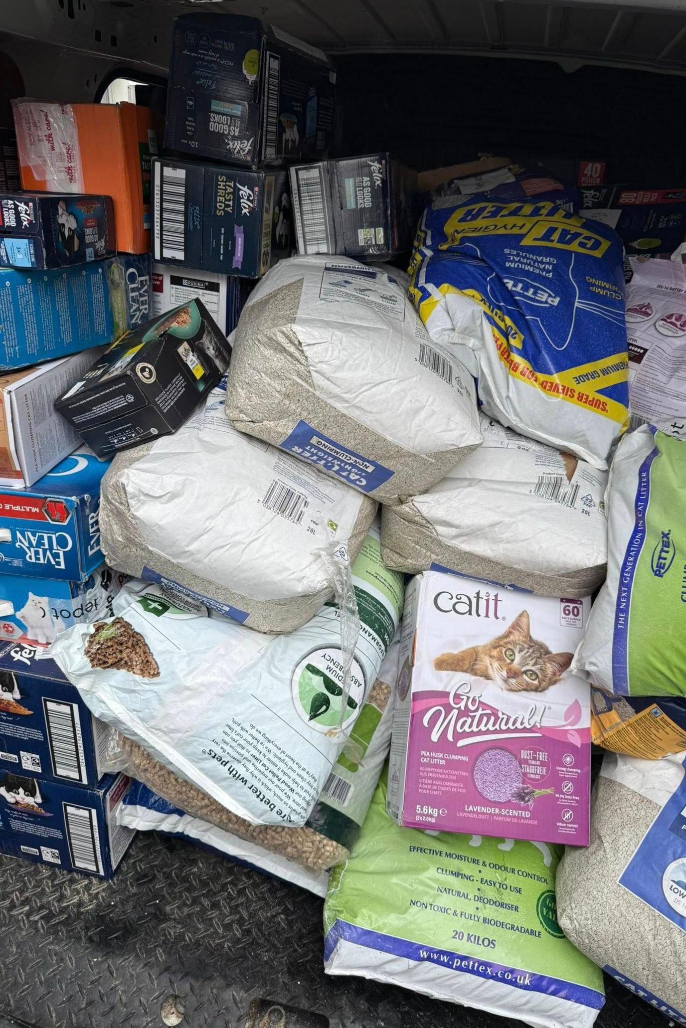 A van with its back doors open showing it piled high with boxes and sacks of cat food and litter.