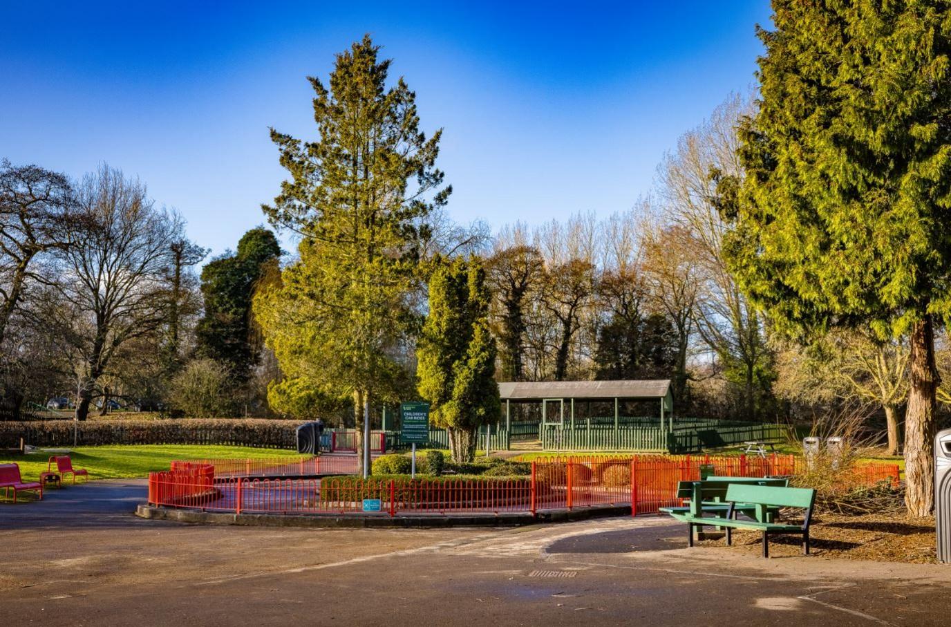 Image of Markeaton Park. There are trees and red fencing close to a pavilion-like structure.