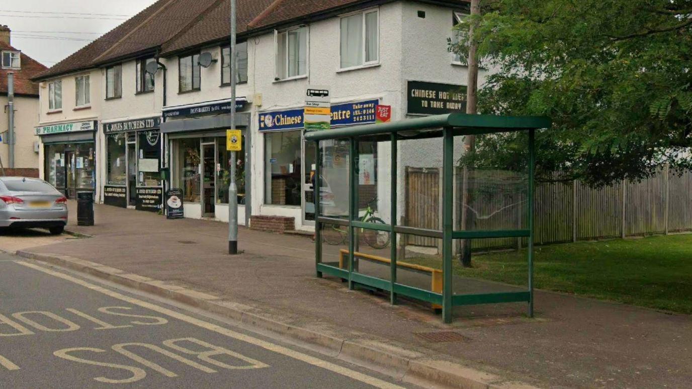 the bus stop and shelter on a road with some shops behind