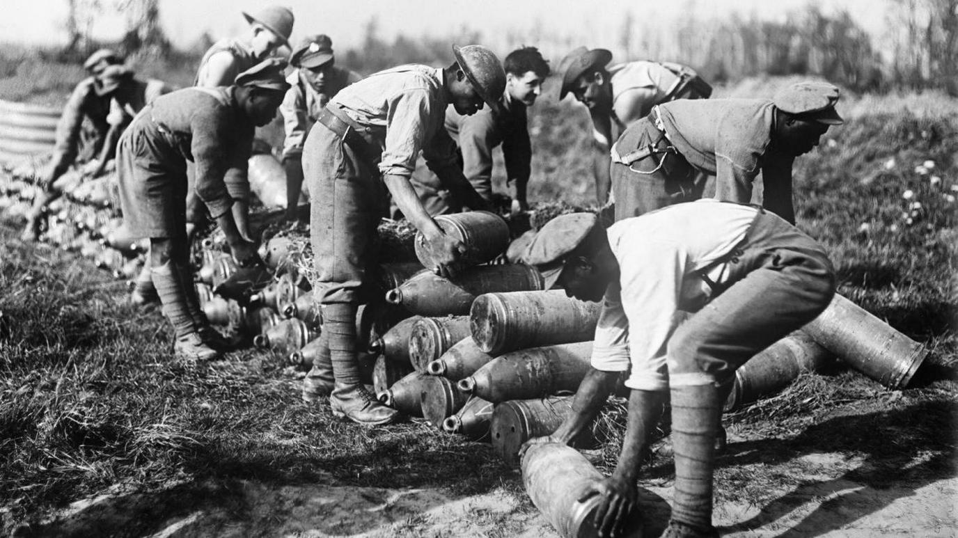 A black and white photo of men in World War One stacking bomb casings