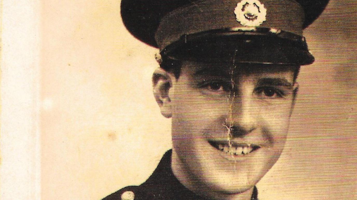A black and white photo of Donald Butt when he was younger and in the Royal Marines. He is wearing his uniform and smiling.