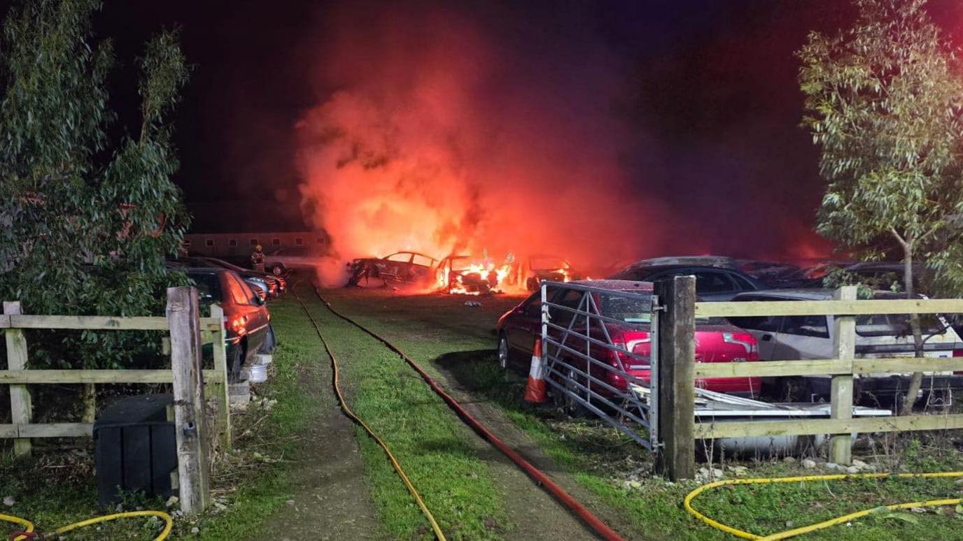 Cars on fire in a farmyard with smoke blowing up into the air