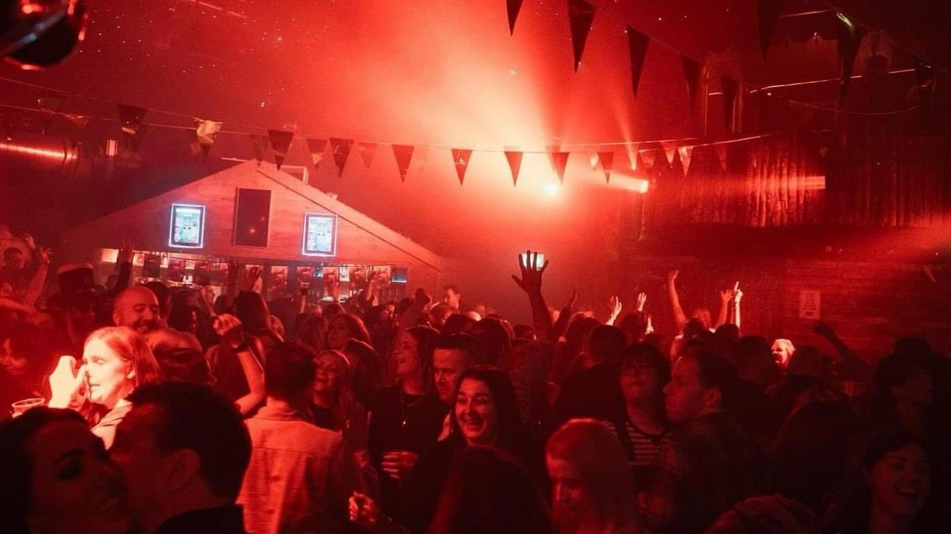 Interior of nightclub The Shed with a large crowd and bright red lights