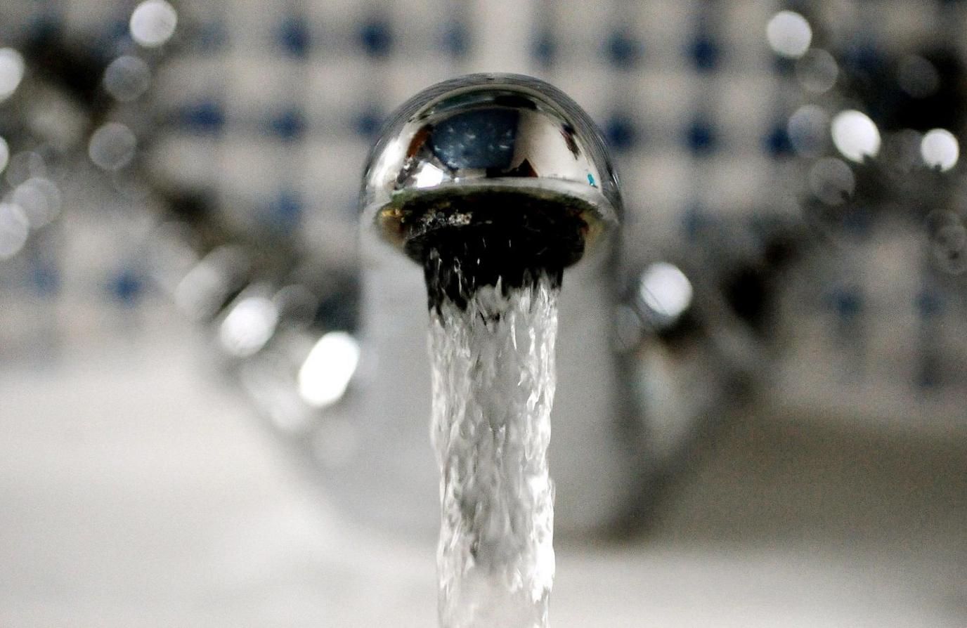 A close up of a chrome tap with water pouring out of it.