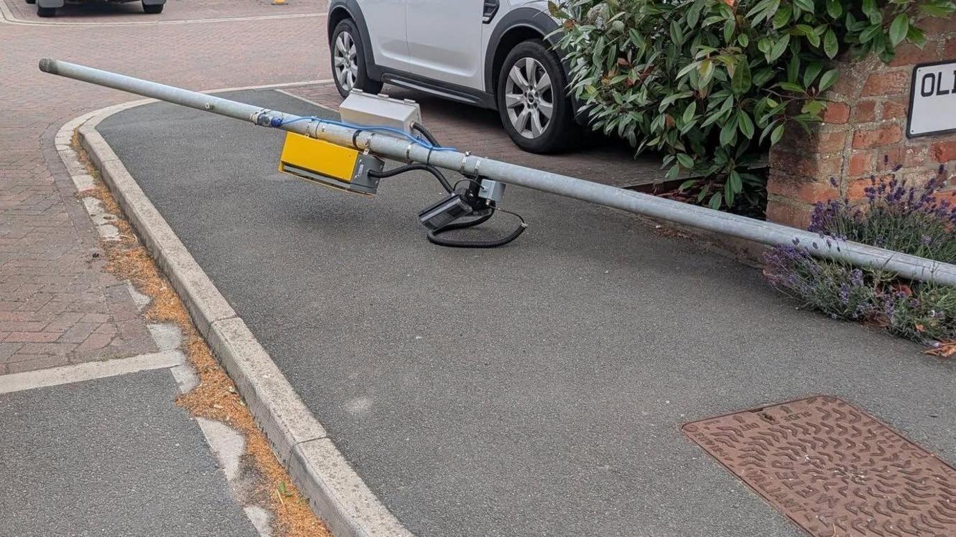 A lamppost, knocked over, with a speed camera attached to it.