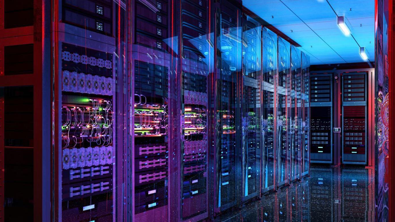 A purple, pink and blue glow surrounds rows of data centre server racks. There are several wires, folders and slots behind glass doors. The floor is clean and reflects the racks.