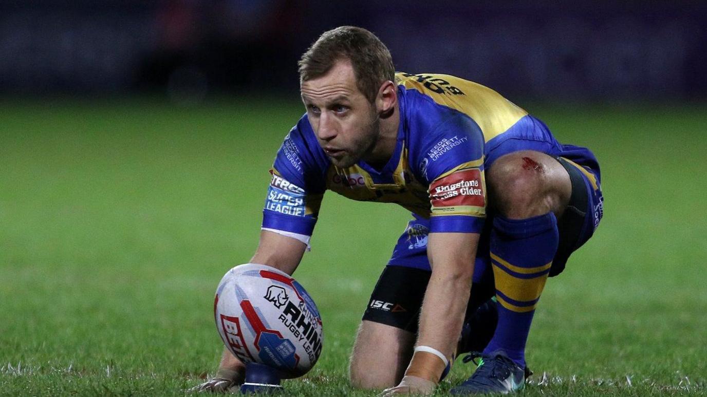 Rob Burrow in his blue and yellow Leeds Rhinos kit as he prepares to kick a ball on a green pitch