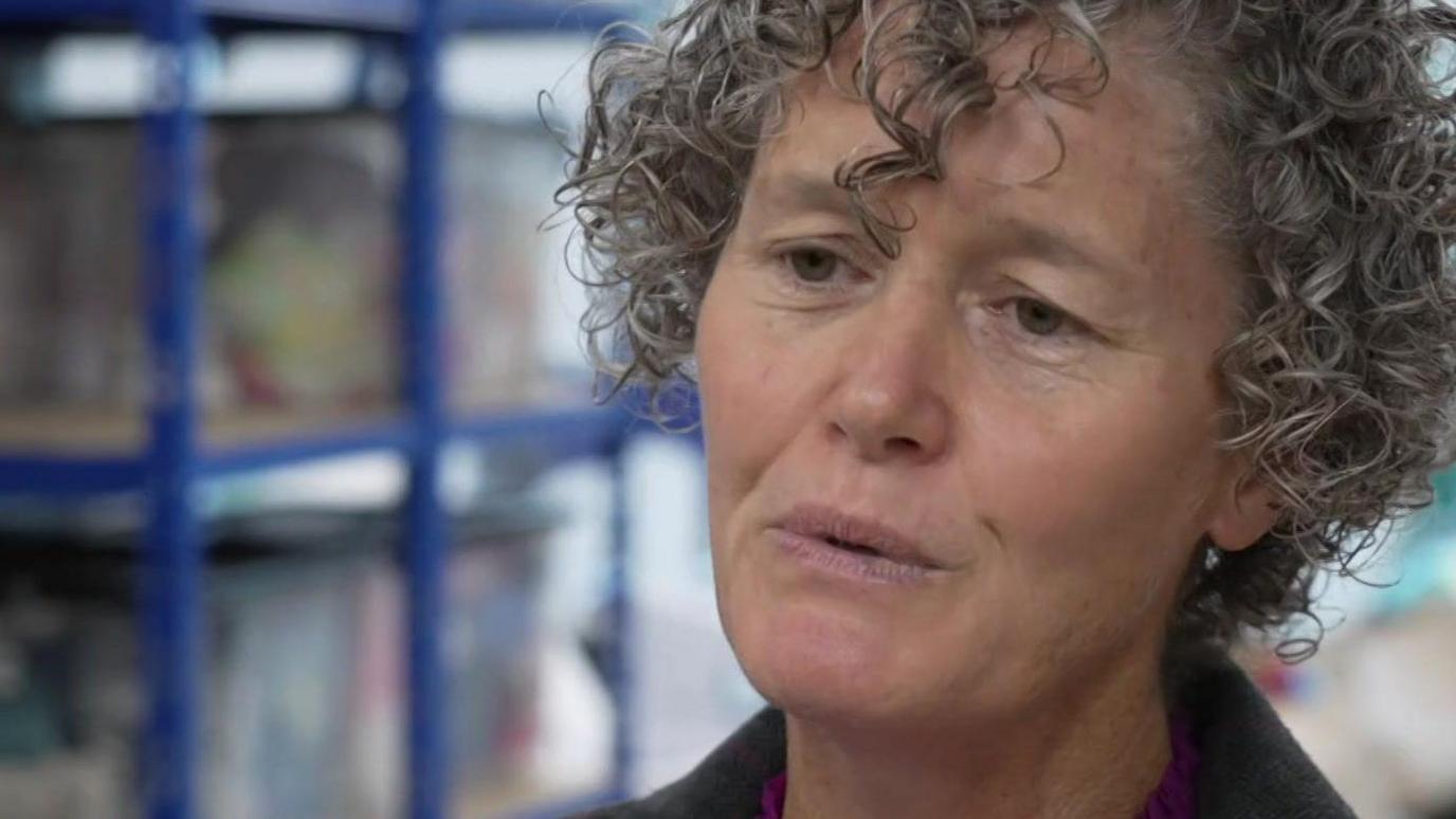Jacqui Scott a curly haired woman wearing a brown blazer and a purple top