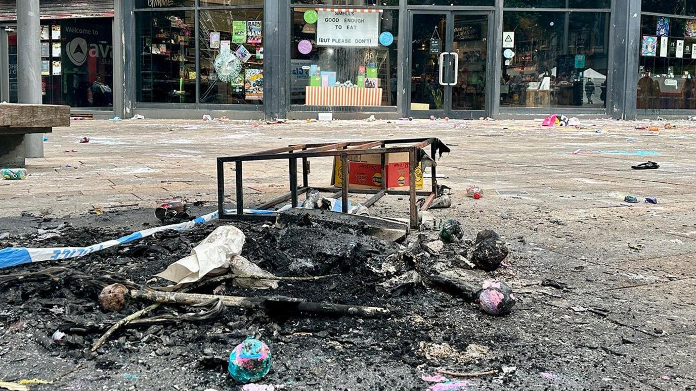 Black and charred and burnt out rubbish in front of a glass-fronted shop