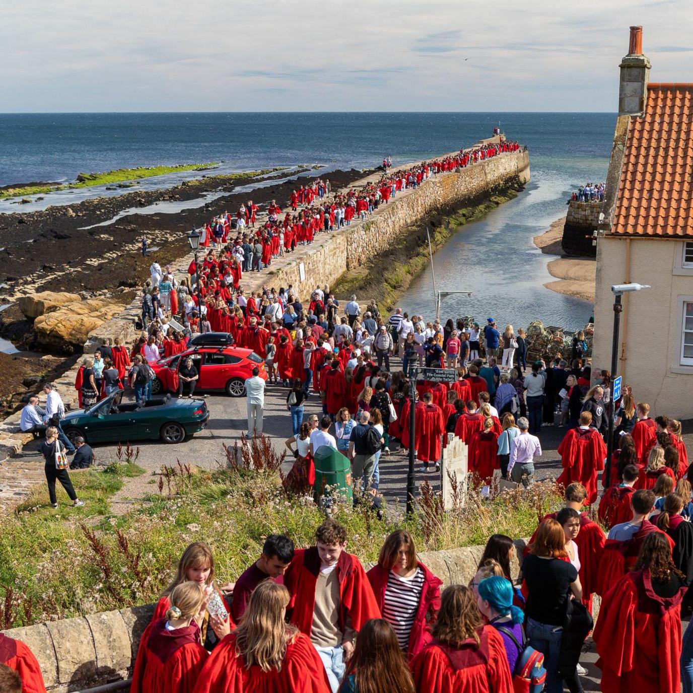 Lots of people in red gowns walking across the long pier