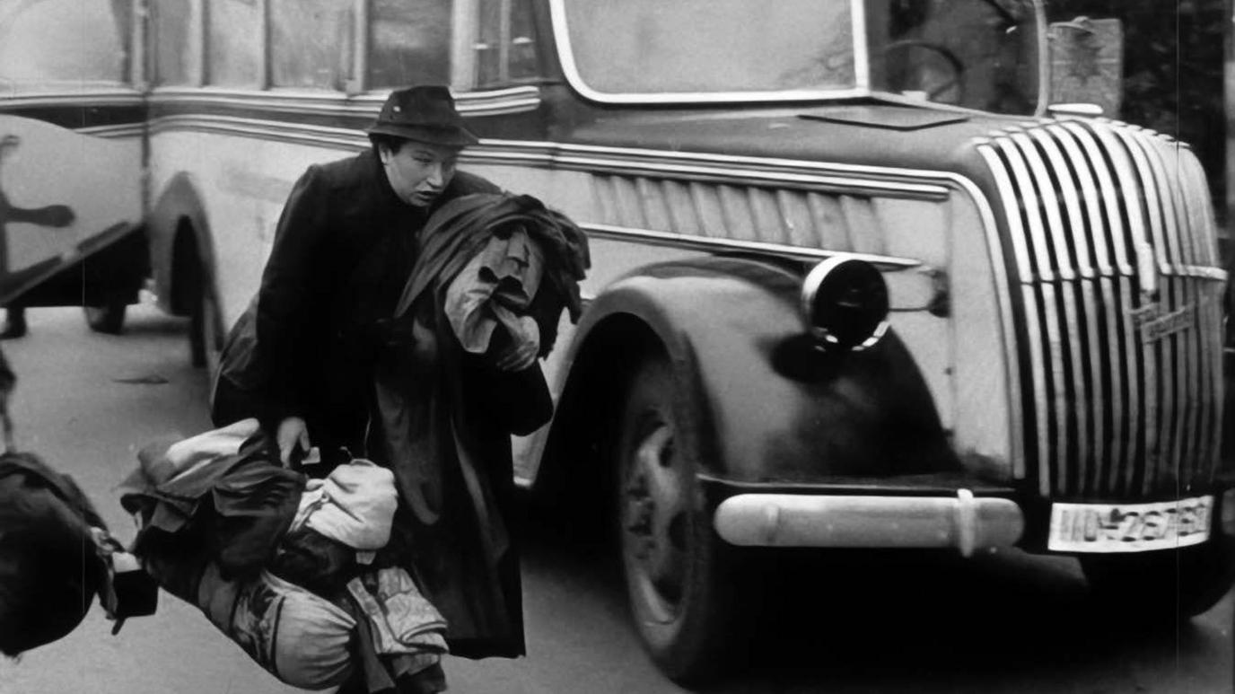 Llun du‑a‑gwyn o Ebrill 1942 yn dangos menyw - Mira Marx - yn cario ei heiddo olaf wrth gerdded heibio bws mawr metelaidd. Mae dillad a bwndeli trwm yn hongian o’i breichiau, gan gyfleu brys ac anobaith.