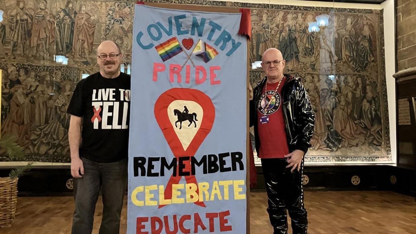 Two men standing next to an Aids memorial quilt