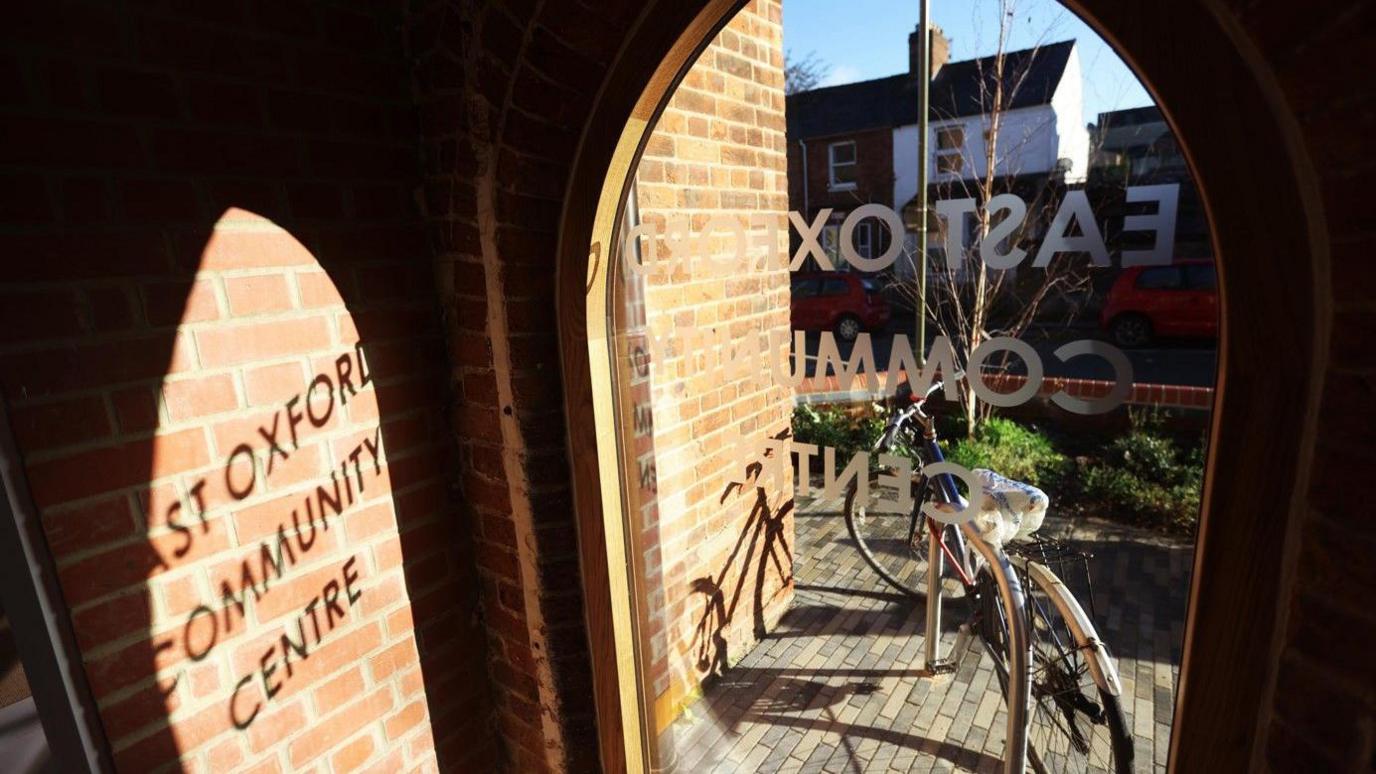 A view from inside the building of an arched window. The words "East Oxford Community Centre" are printed on the glass.