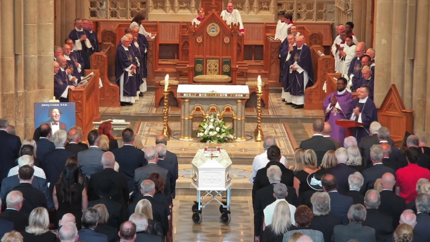 People at Salford Cathedral sit on pews as a coffin is at the front