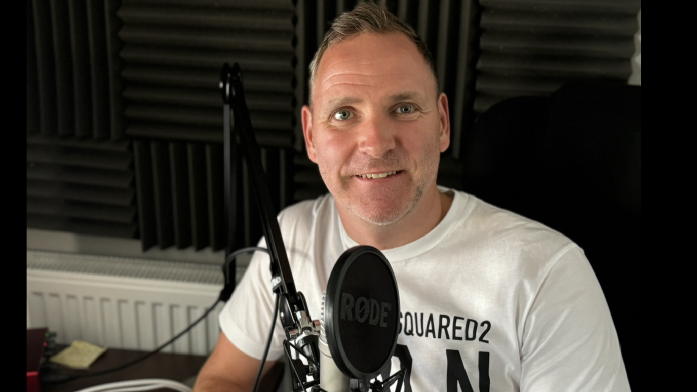 Podcaster Dean Booty sitting in a studio in front of a microphone