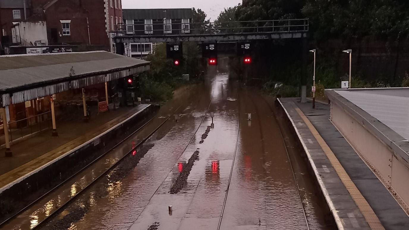 Brown flood water submerging train tracks next to two platforms