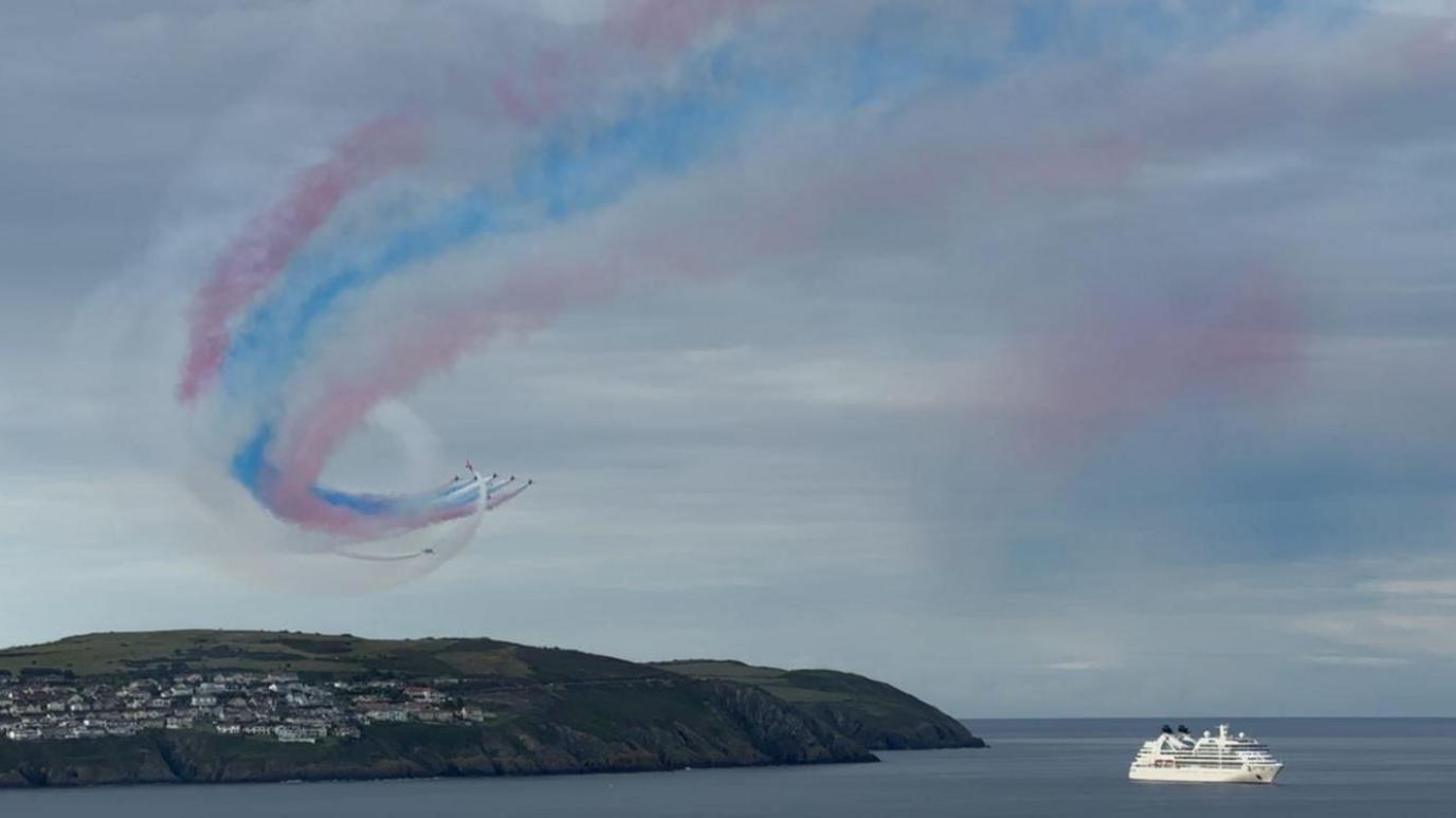 A white cruise ship in the bay with the red arrows above.
