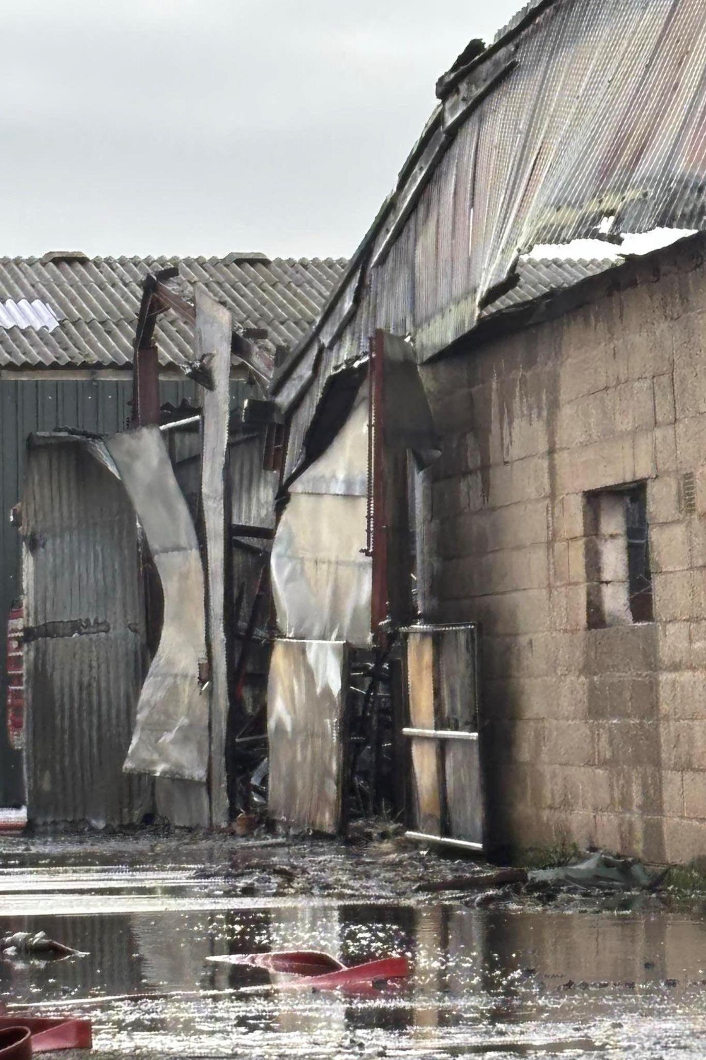 A close-up of a fire-damaged building with a buckled roof, parts coming away and water around the walls after the firefighters put out the blaze.