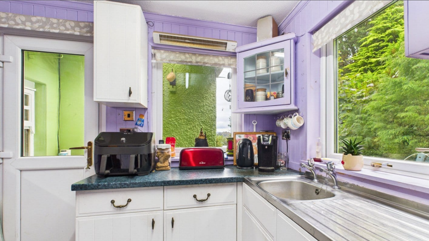 Estate agent's photo of the kitchen in Beul An Atna with purple interior walls and green exterior walls visible through the windows.