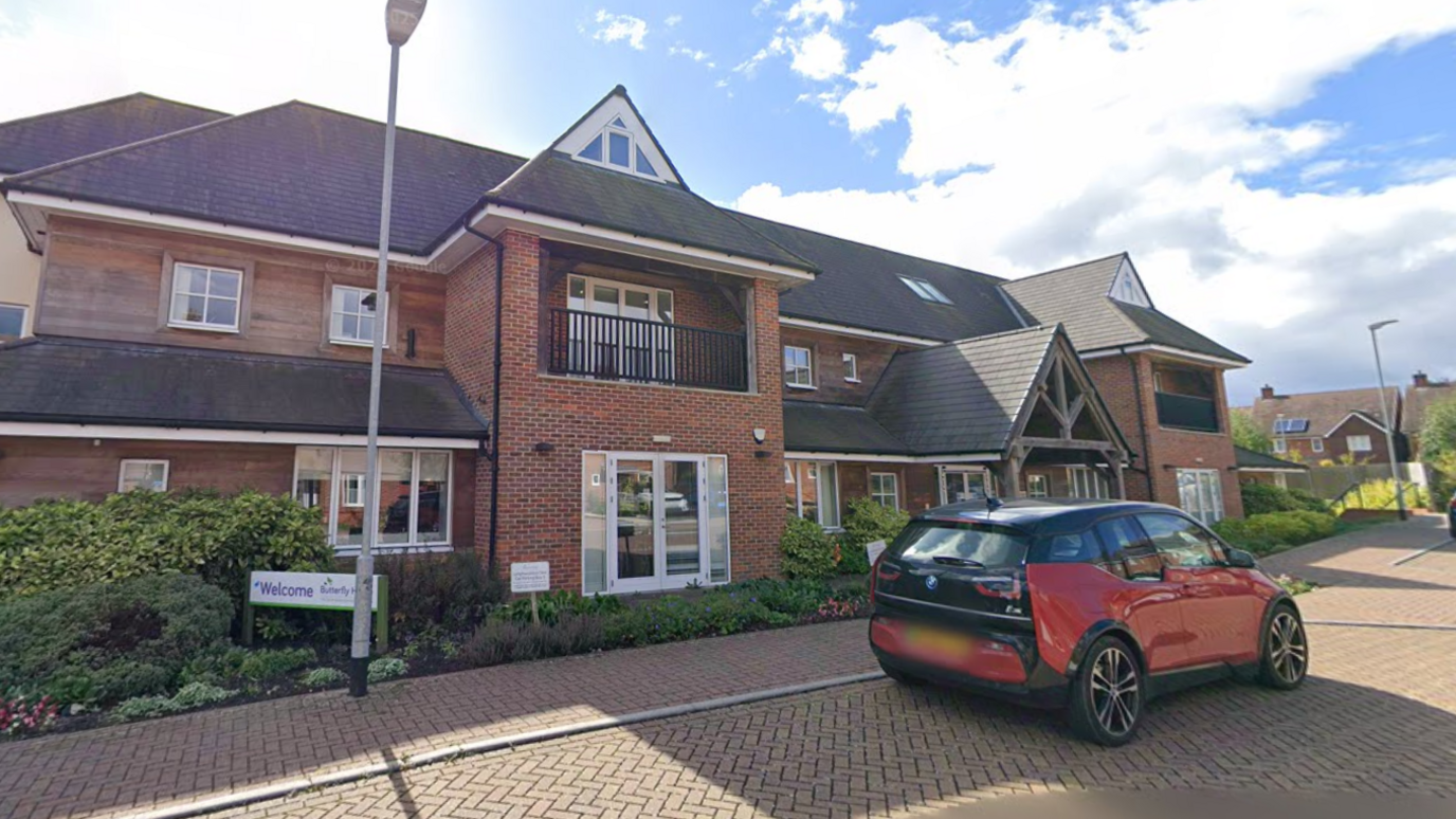 A hospice building with a red car parked outside.