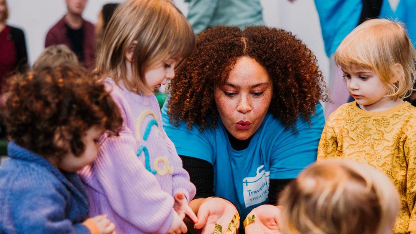 A Trinity Arts worker demonstrating a toy to children who are looking on