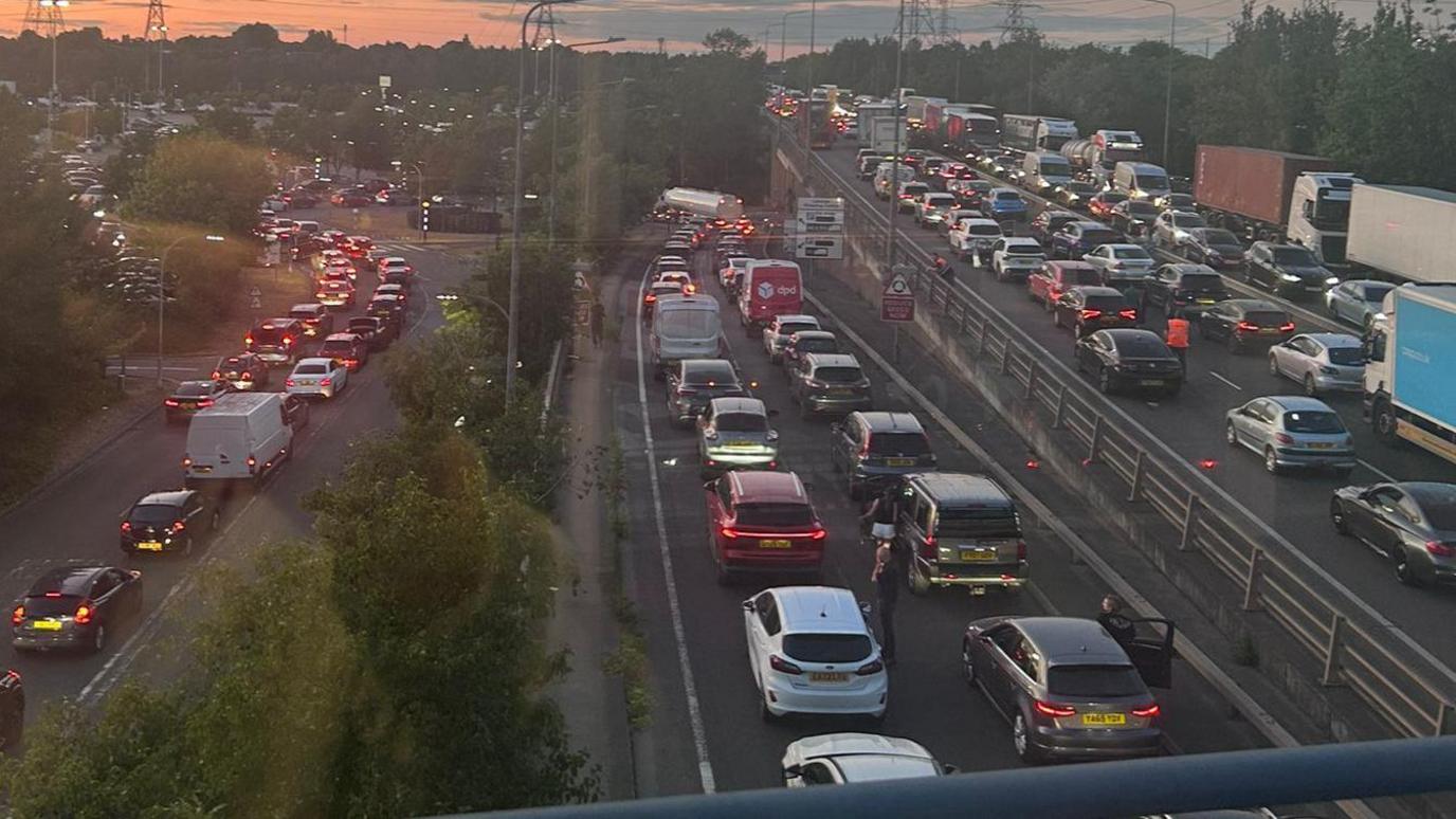 This picture taken from a bridge above a road shows three different roads, all dual-carriageway, gridlocked. Cars, vans and lorries are top to tail queuing during dusk. The queues are huge and cover the entire picture.
