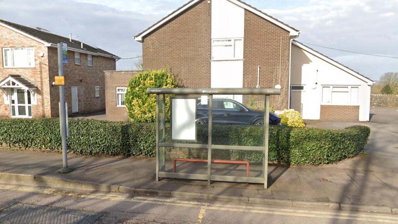 A google street view image of a bus stop shelter by the side of the road.