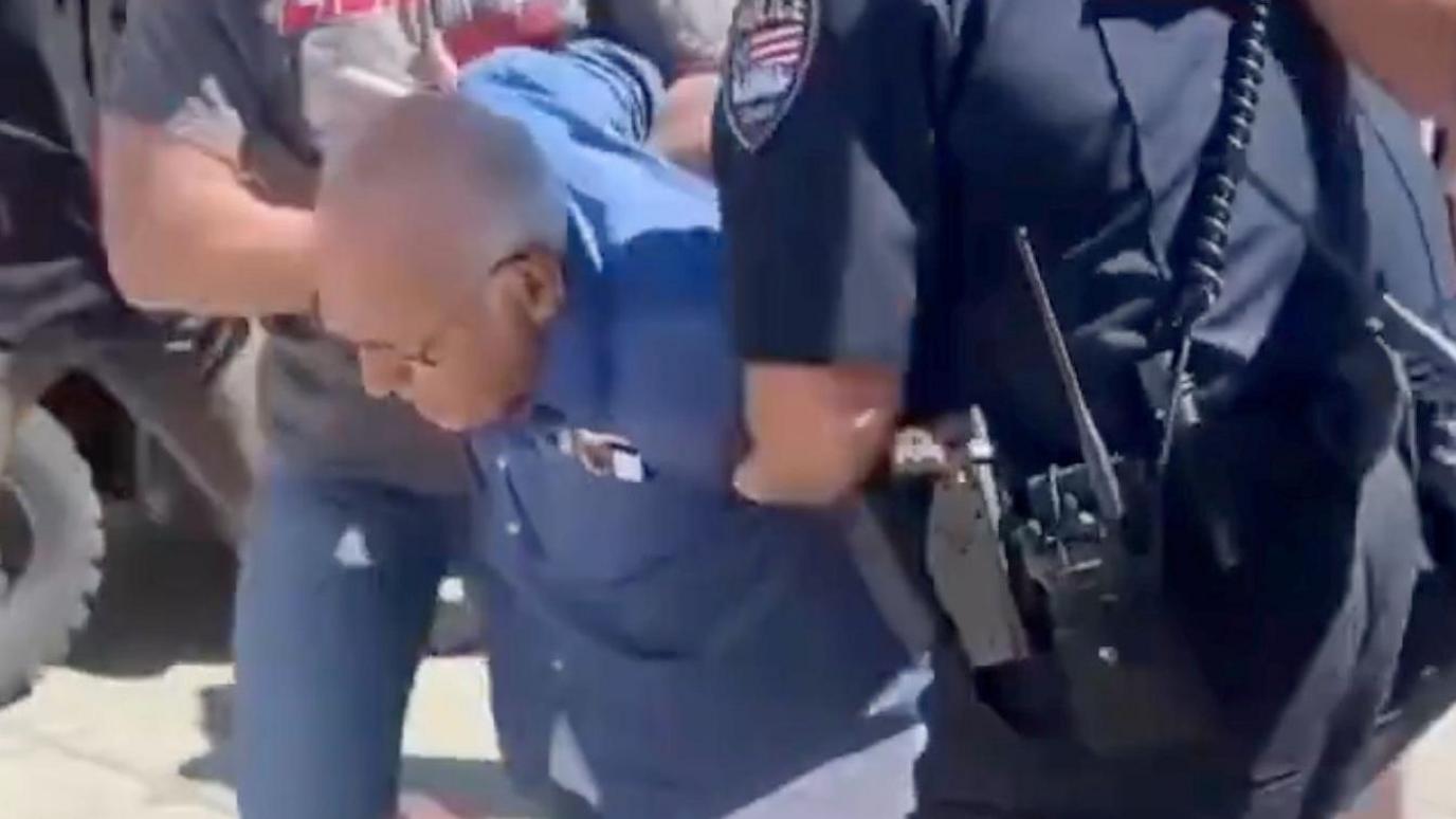A man in a blue shirt being held by police officers
