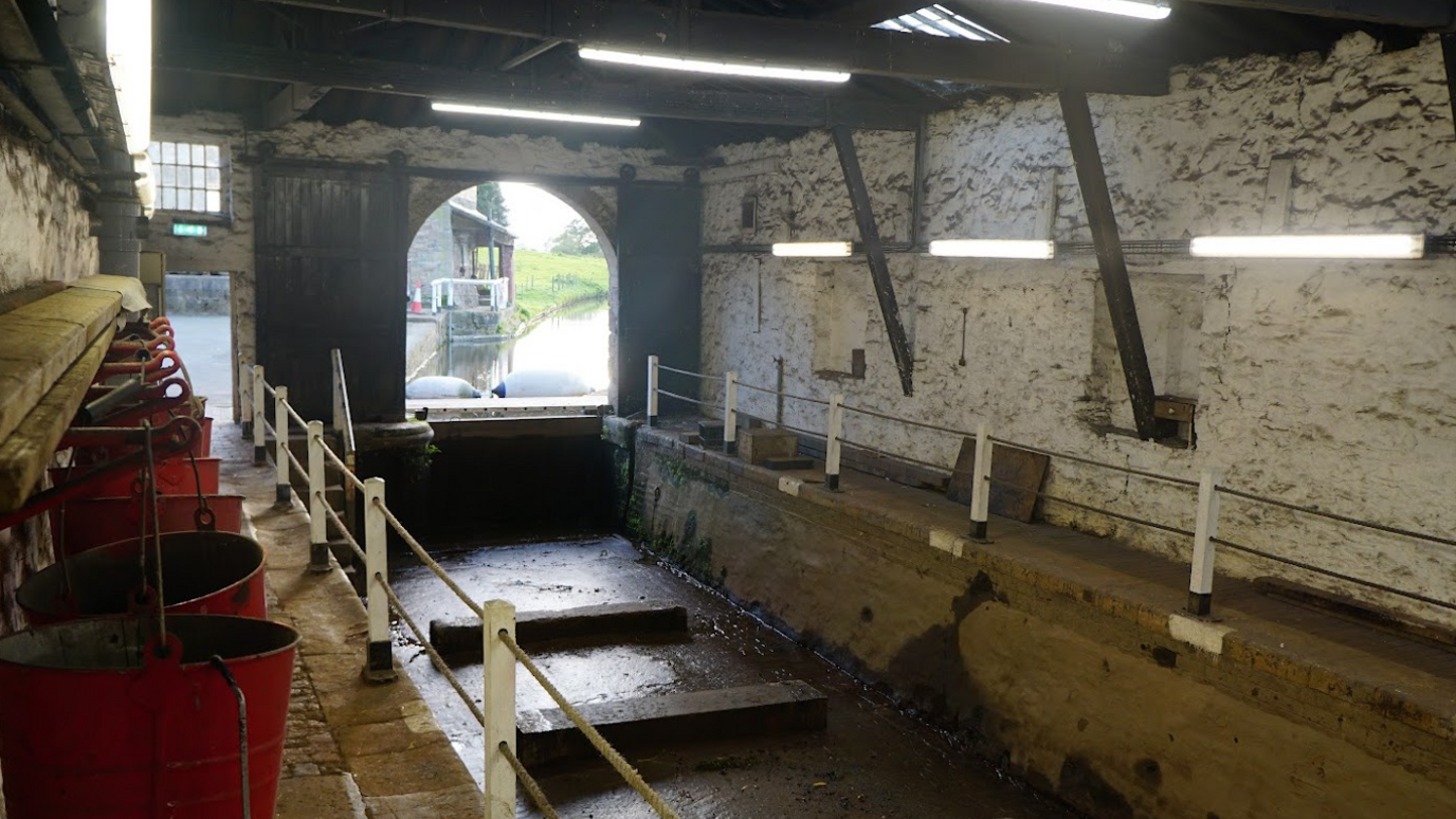 The photo shows inside a building where boats are worked on with a low ceiling and old stone whitewashed walls