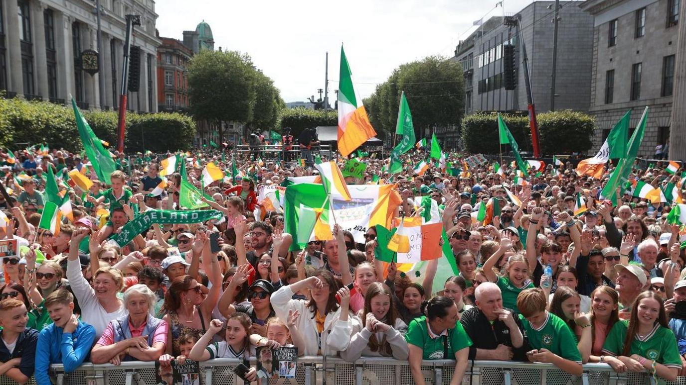 Crowd of people, many wearing Ireland tops and waving tricolours, in Dublin's O'Connell Street 