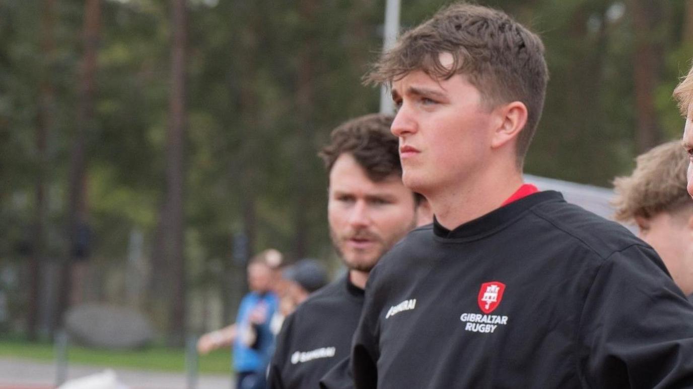 Llun o Sean Magee yn edrych i ffwrdd. Mae'n gwisgo top hyfforddi tim rygbi Gibraltar.