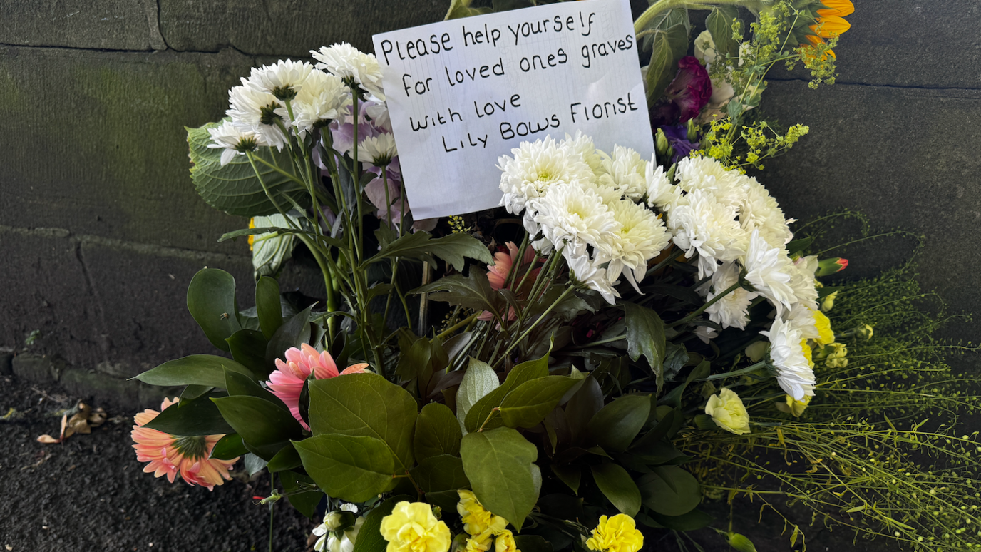 A bucket containing flowers and a sign saying 'please help yourselves for loved ones graves'