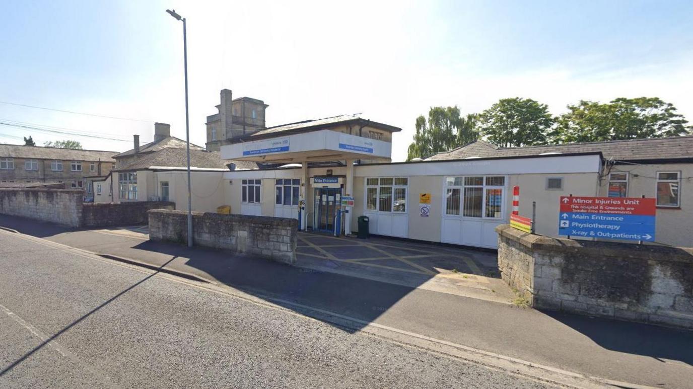 The entrance of the Trowbridge Community Hospital - a flat-roofed, tired building with a lot of signage. Lamppost outside.