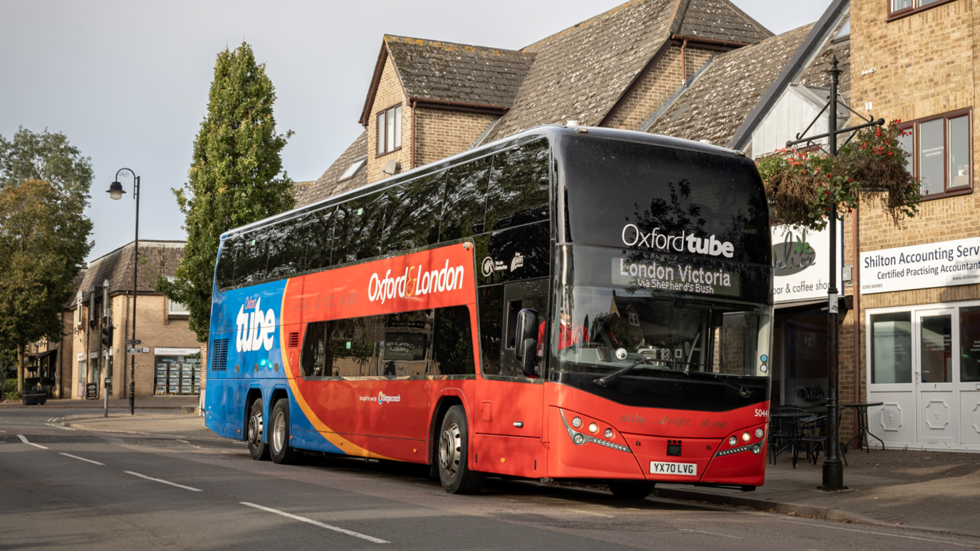 a red and blue bus with Oxford Tube written on the front, driving along a road with buildings to its left hand side