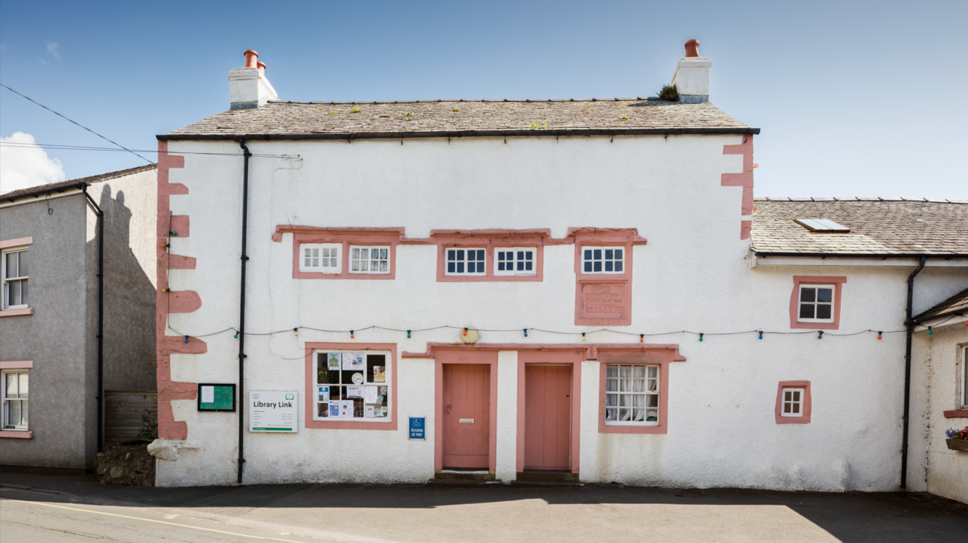 A white building with a slate cobbled roof. There are small windows at the front with pink bricks.
